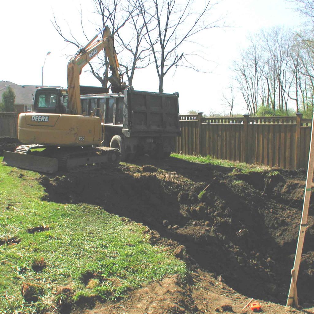 Excavator digging a back yard and loading a dump truck