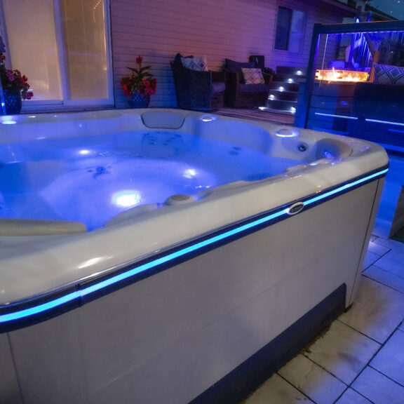 Close up of a corner of a hot tub with a glow of blue lights around the side of the hot tub.